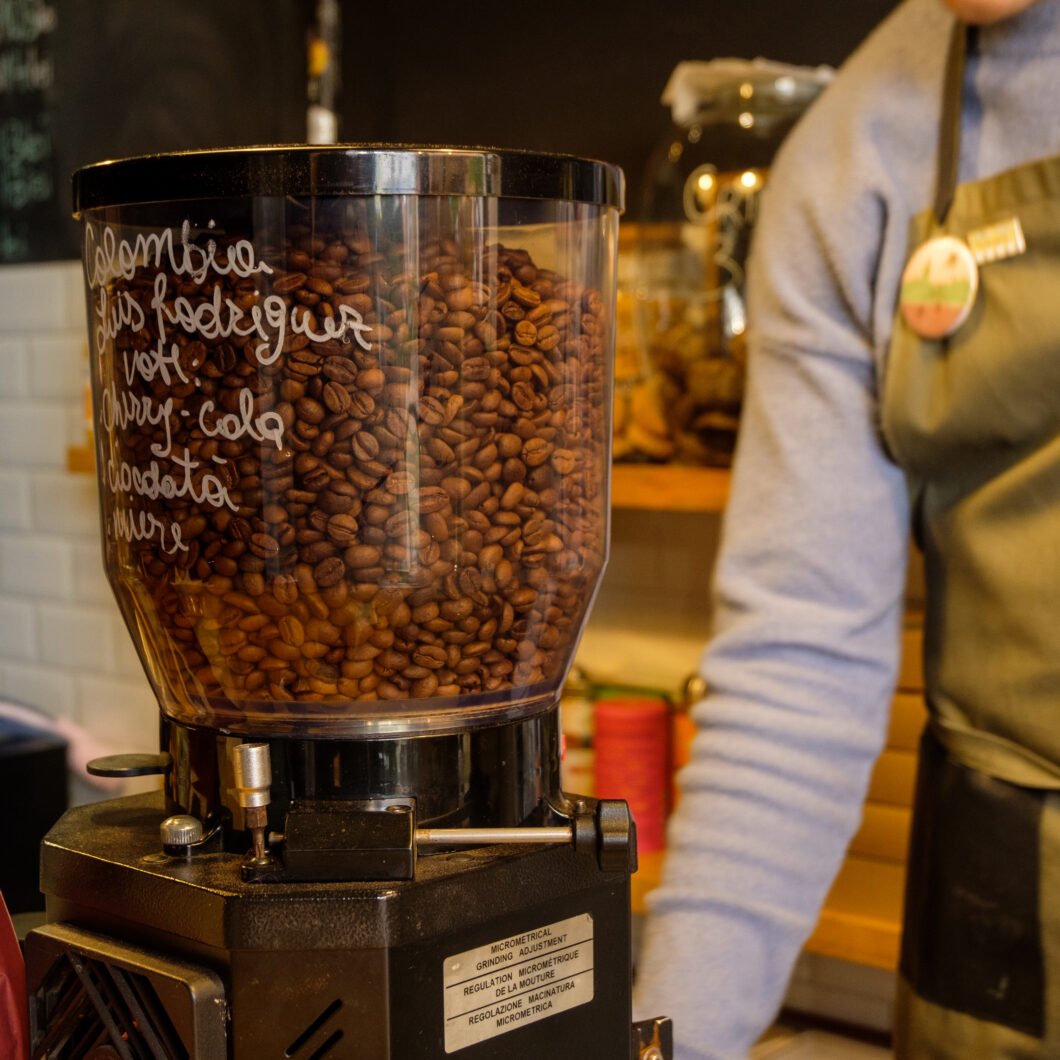 A barista near a glass of coffee beans in the black coffee machine, ambiental coffee shop