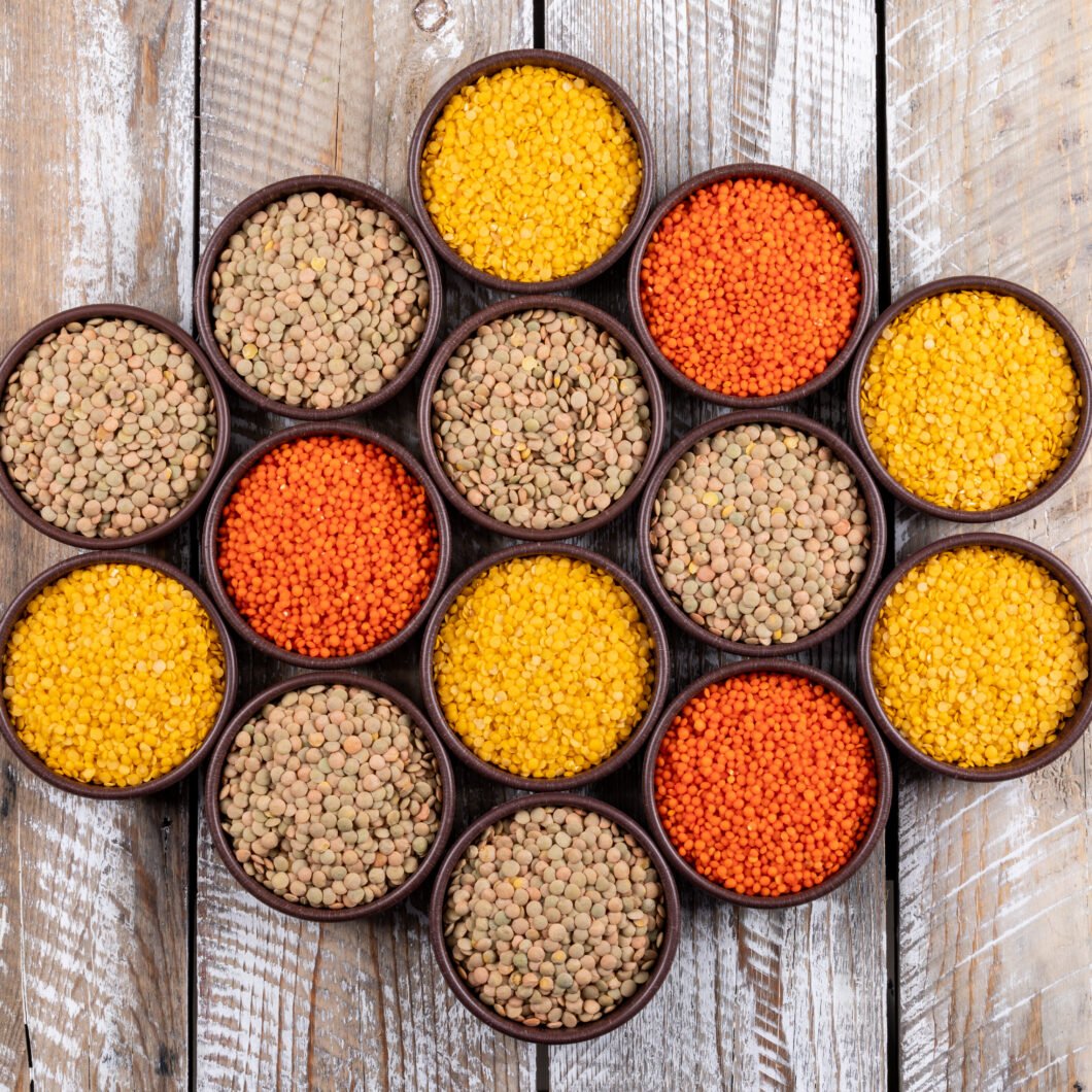 Set of redf, yellow, green lentils and different lentils in a brown bowls on a beige wooden background. top view.